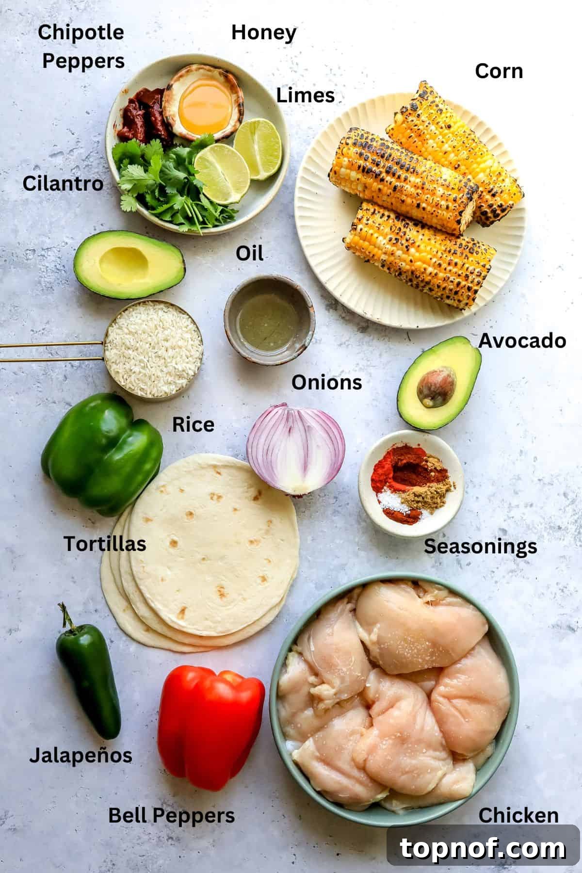 Fresh ingredients laid out on a white countertop, including sliced chicken, bell peppers, onions, and various spices in bowls, ready for cooking.