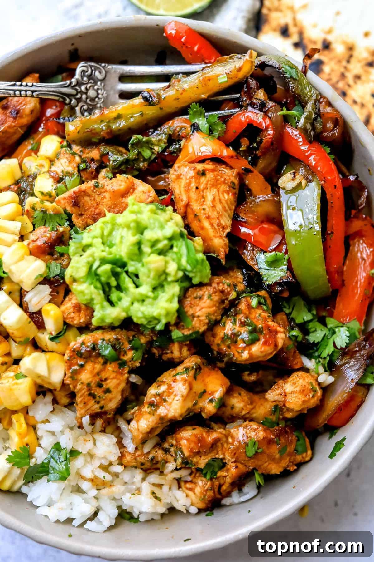 Close-up of a grey bowl filled with chicken fajita, fluffy white rice, topped with fresh guacamole and a sprinkle of cilantro.