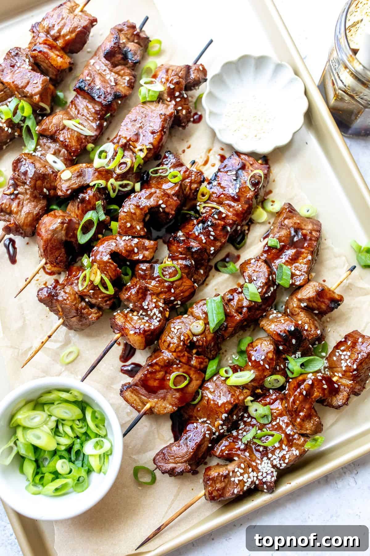 Aromatic Garlic Ginger Beef Skewers 2 A baking sheet with beautifully cooked steak skewers, glistening with sauce and garnished with fresh green onions.
