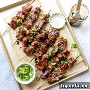 A baking sheet with beautifully cooked steak skewers, glistening with sauce and garnished with fresh green onions.