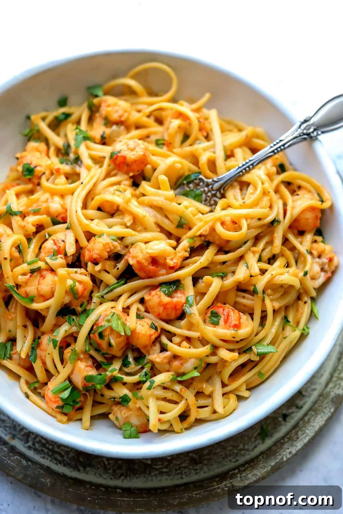 A pristine white bowl filled with creamy lobster pasta, garnished with fresh parsley, with a silver fork resting on the side, inviting a delightful meal.