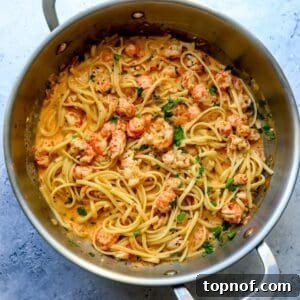 Stainless steel skillet filled with creamy lobster pasta, garnished with fresh herbs, ready to be served.