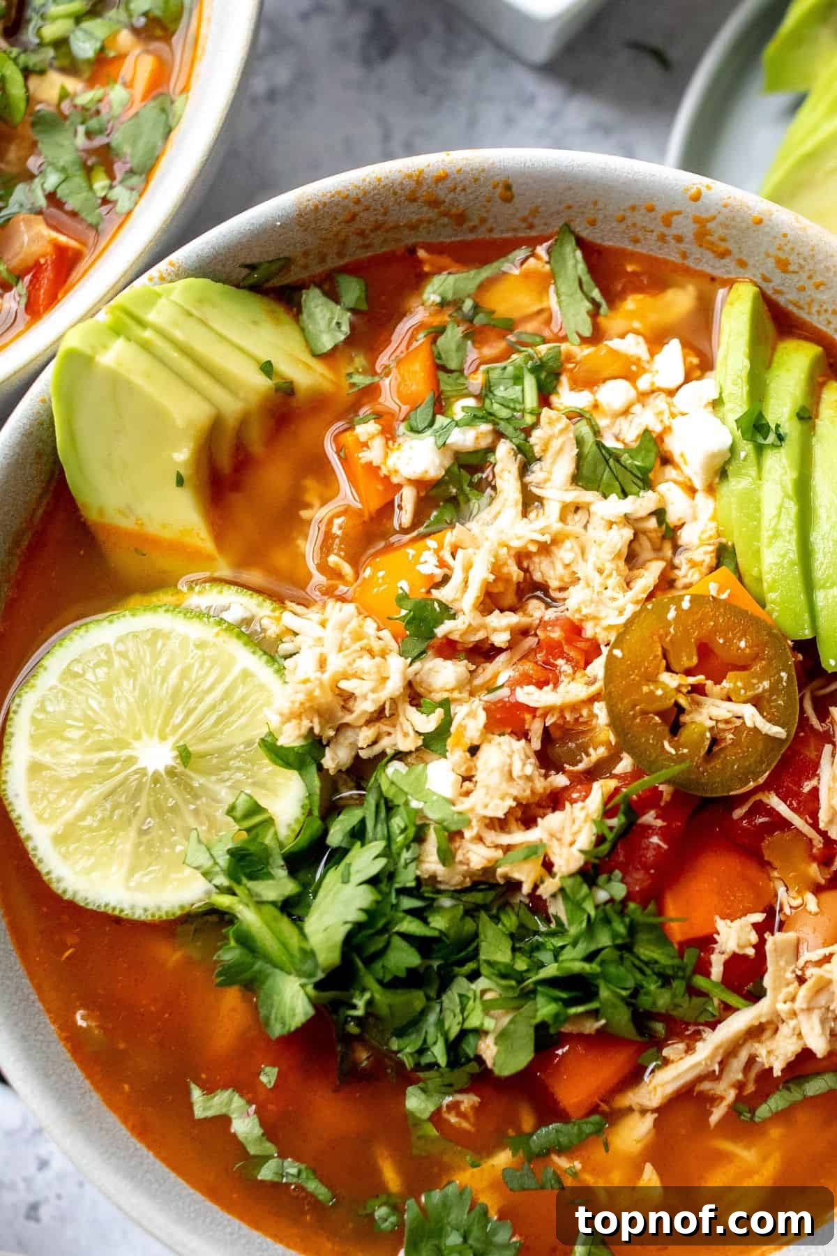 Zesty Chicken Lime Fiesta Soup 5 Close-up view of a ceramic bowl filled with brothy Mexican Chicken Lime Soup, garnished with fresh avocado and lime wedges, emphasizing its freshness and appeal.
