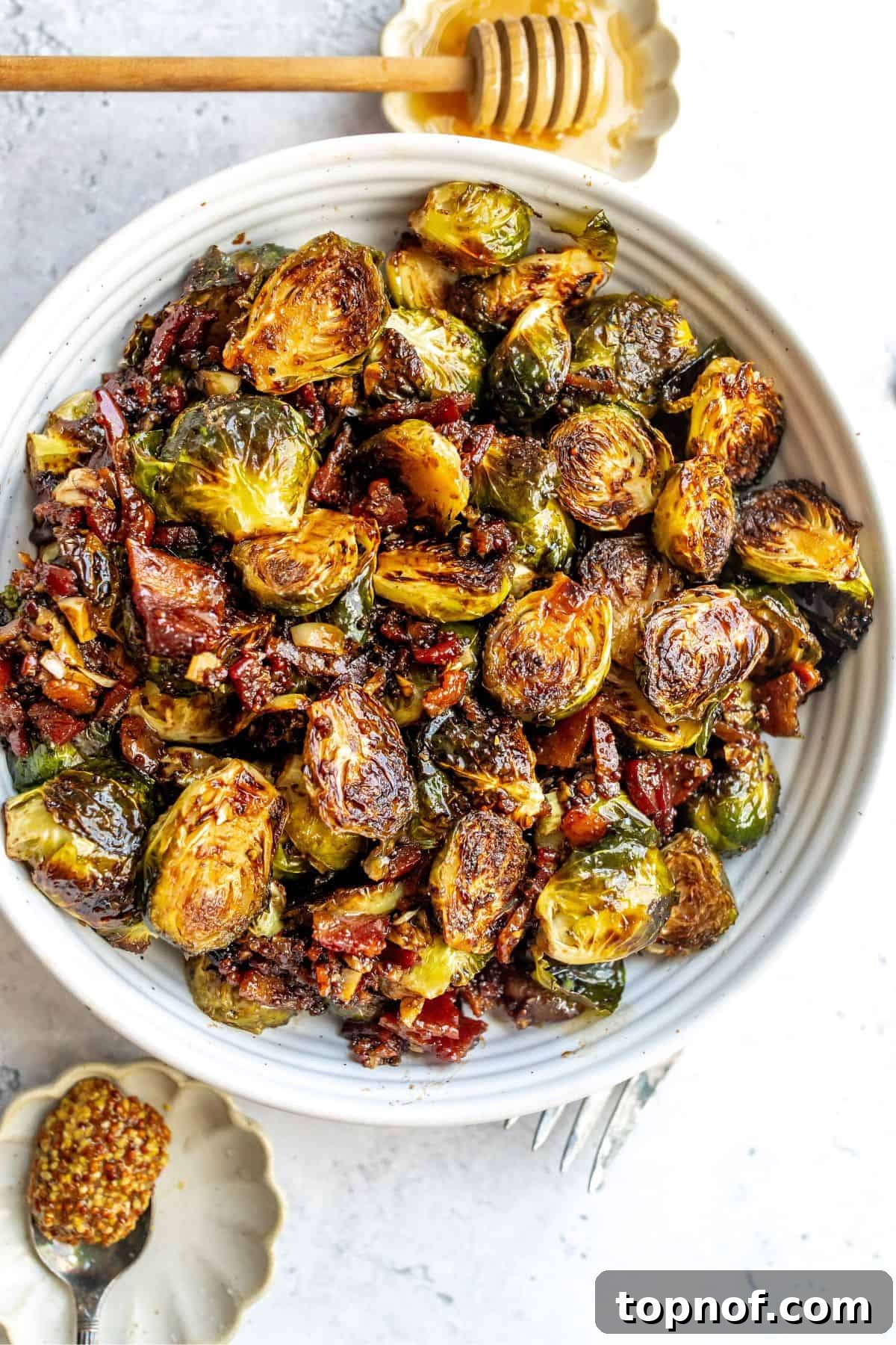 White ceramic bowl filled with roasted Balsamic Honey Brussels Sprouts, garnished with fresh herbs and a drizzle of honey.