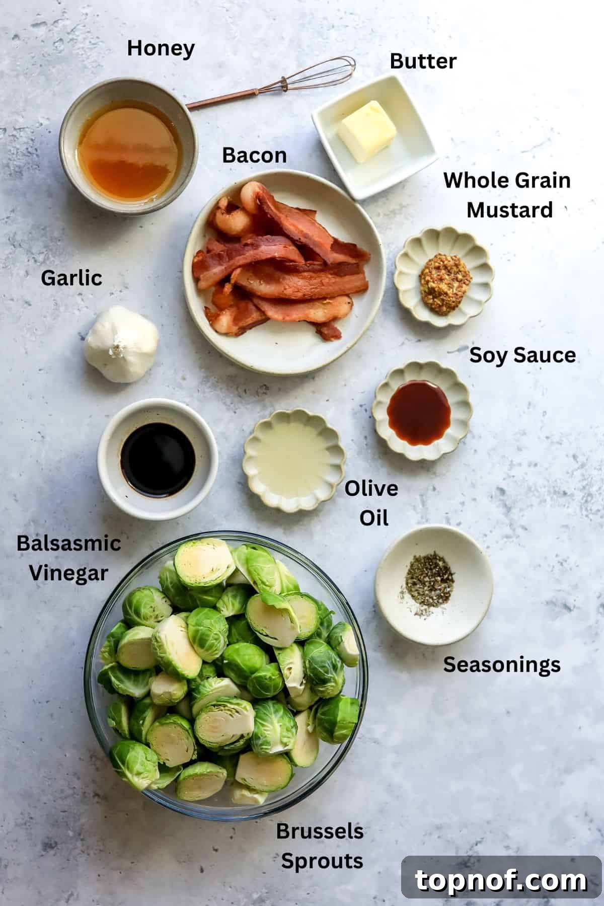 A selection of fresh ingredients including Brussels sprouts, honey, balsamic vinegar, and mustard on a rustic wooden board.