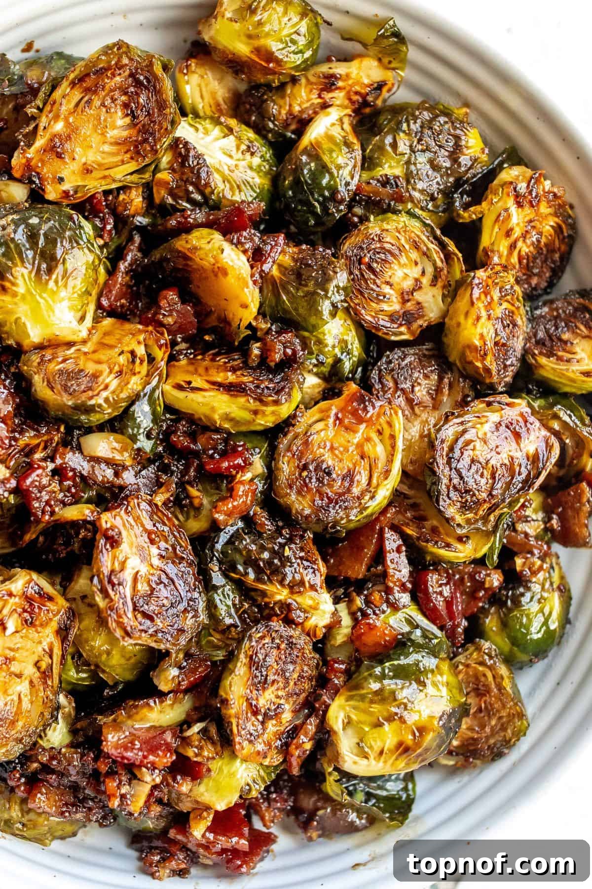 White bowl with Balsamic Honey Brussels Sprouts, garnished with fresh herbs, and a small dish of honey on the side.
