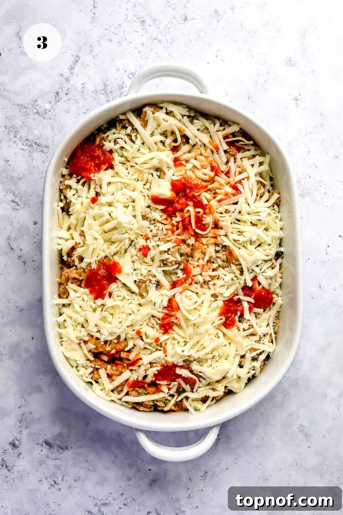 Wholesome Spaghetti Squash Lasagna 5 A white ceramic baking dish filled with the mixed lasagna ingredients, topped with a generous layer of shredded mozzarella cheese, ready for baking.