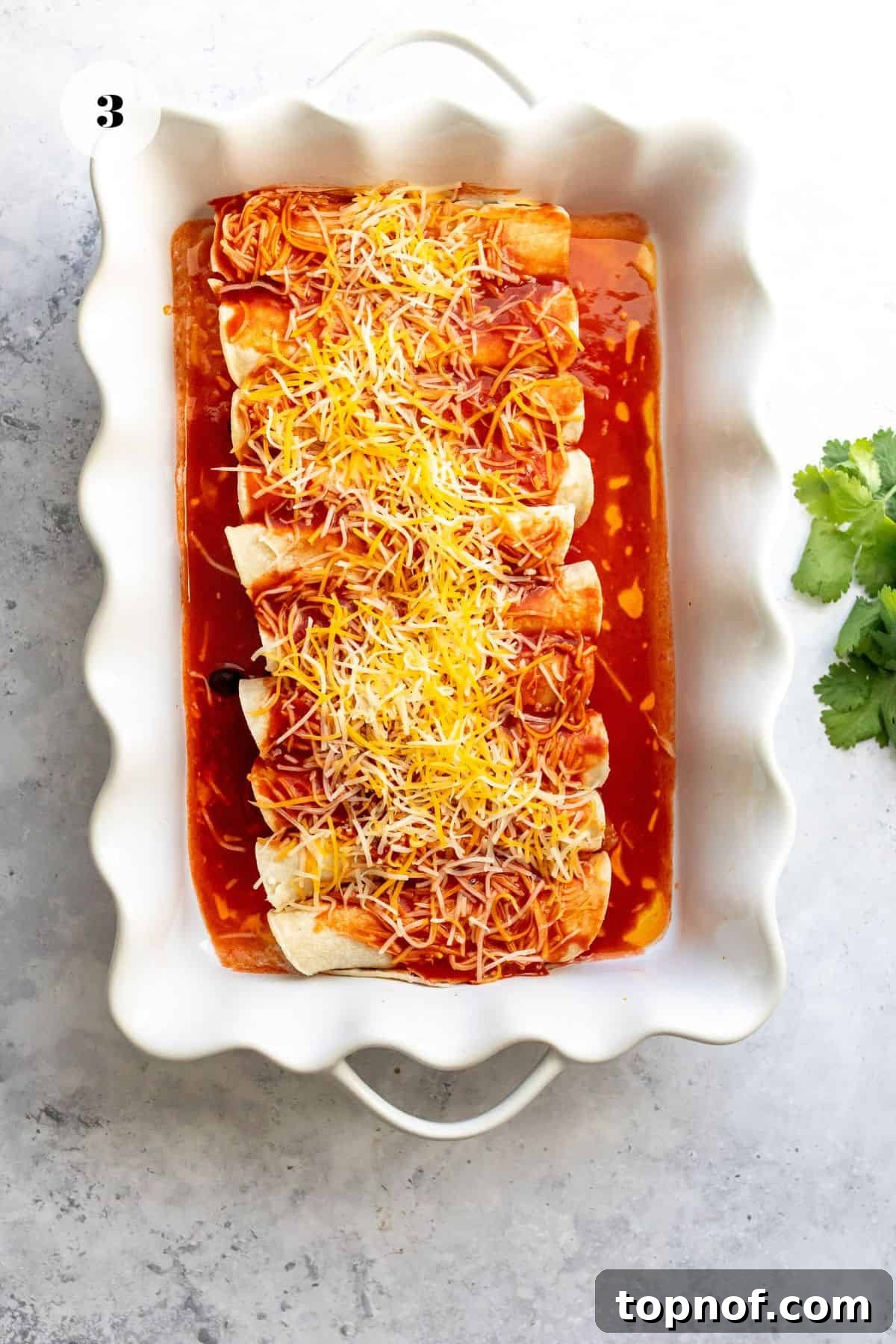 Smoky Butternut Squash Enchiladas 5 Freshly rolled enchiladas arranged neatly in a baking dish, topped with generous amounts of sauce and shredded cheese, ready for the oven.