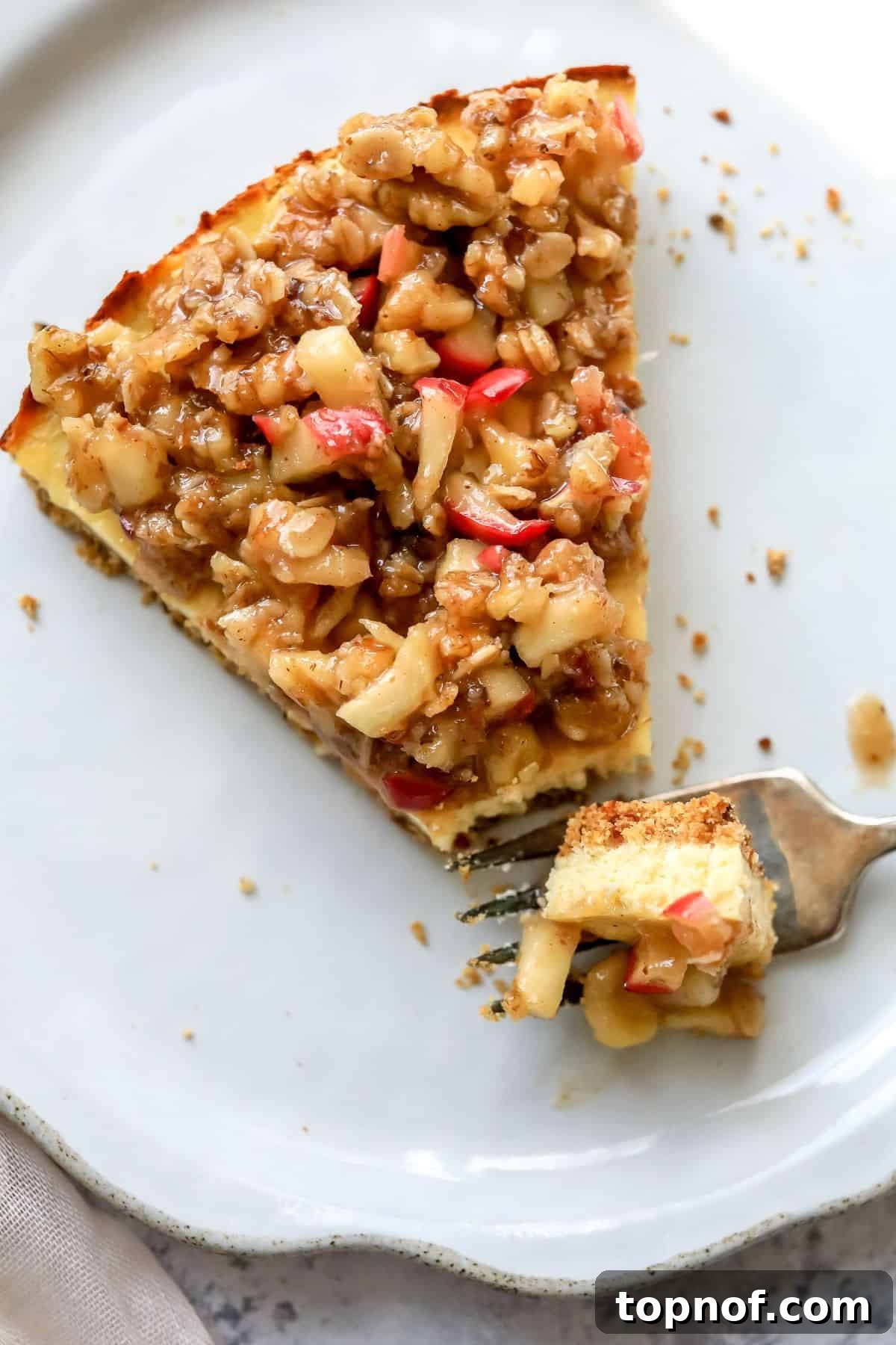 Guilt-Free Protein Cheesecake 2 Cottage Cheese Cheesecake on a white plate with a fork on it. The cheesecake features a golden crust, creamy white filling, and a generous layer of apple crumble topping.