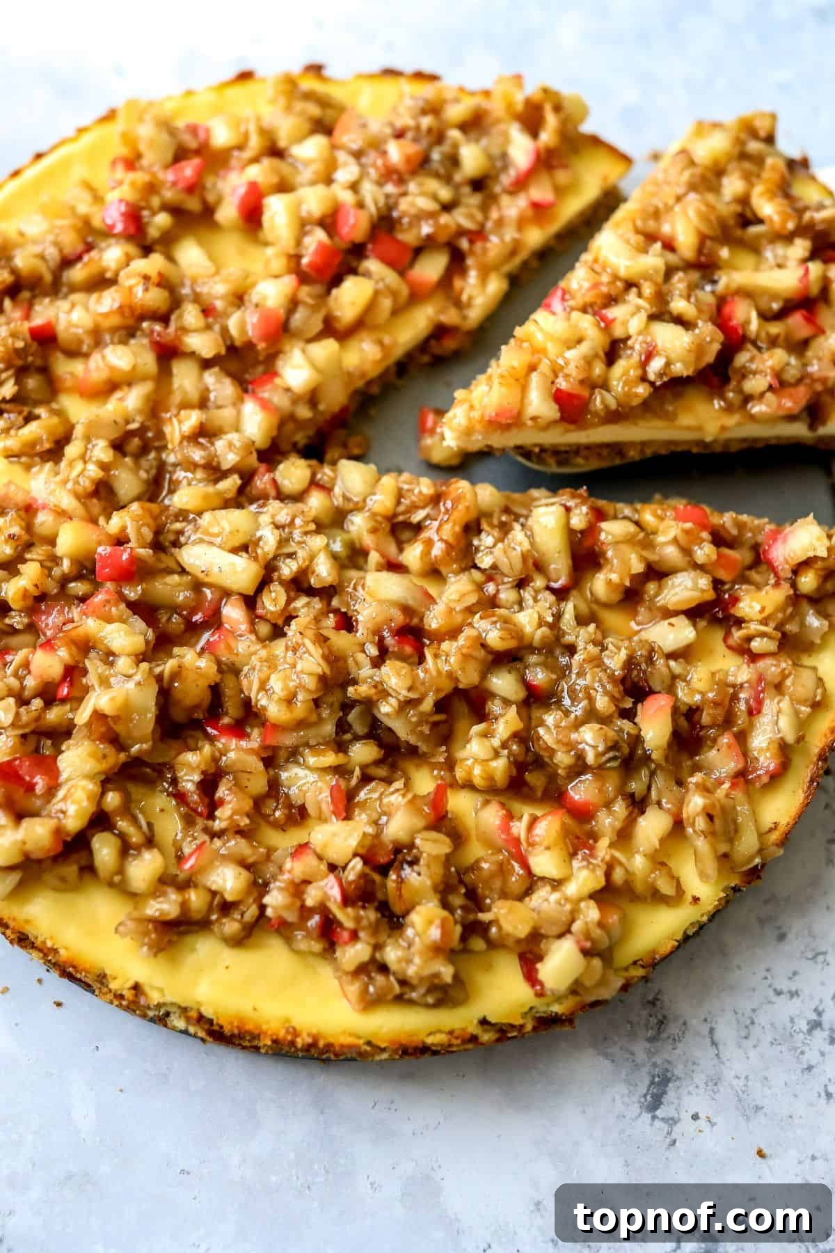 Guilt-Free Protein Cheesecake 6 A slice of protein apple crumble cheesecake, showcasing the layered crust, creamy filling, and abundant topping, served on a white plate with a fork.