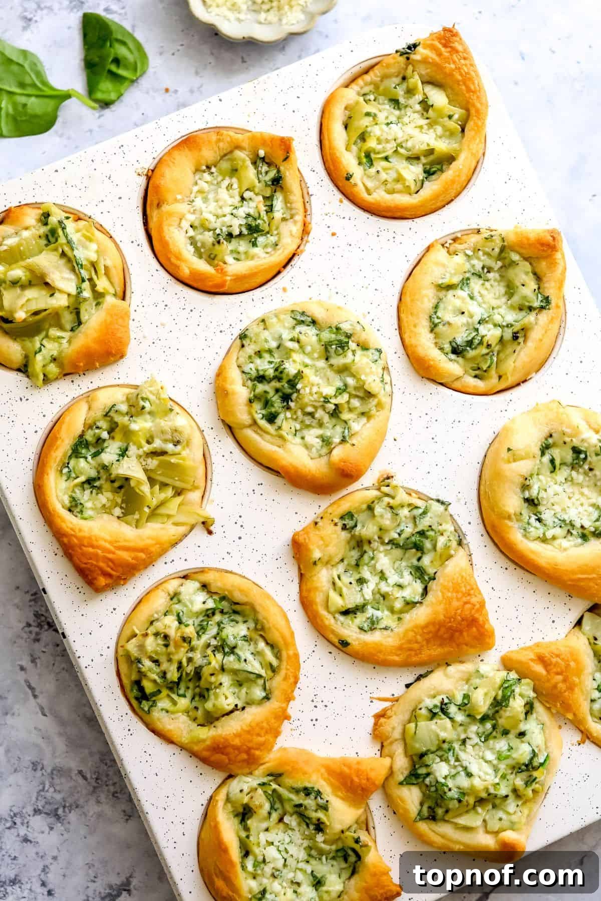 Muffin tin with perfectly baked golden Spinach Artichoke Dip Bites, ready to be served as an appetizer.