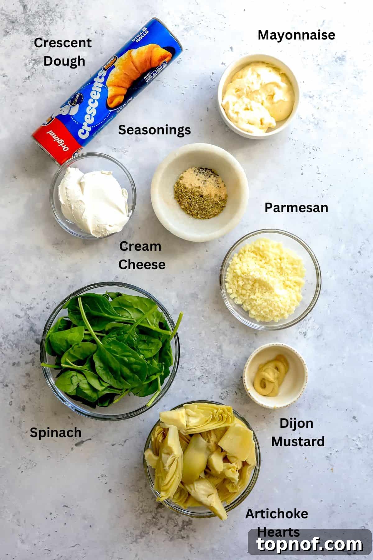 Ingredients laid out on a kitchen counter, showcasing fresh spinach, artichoke hearts, cream cheese, and seasonings in bowls.