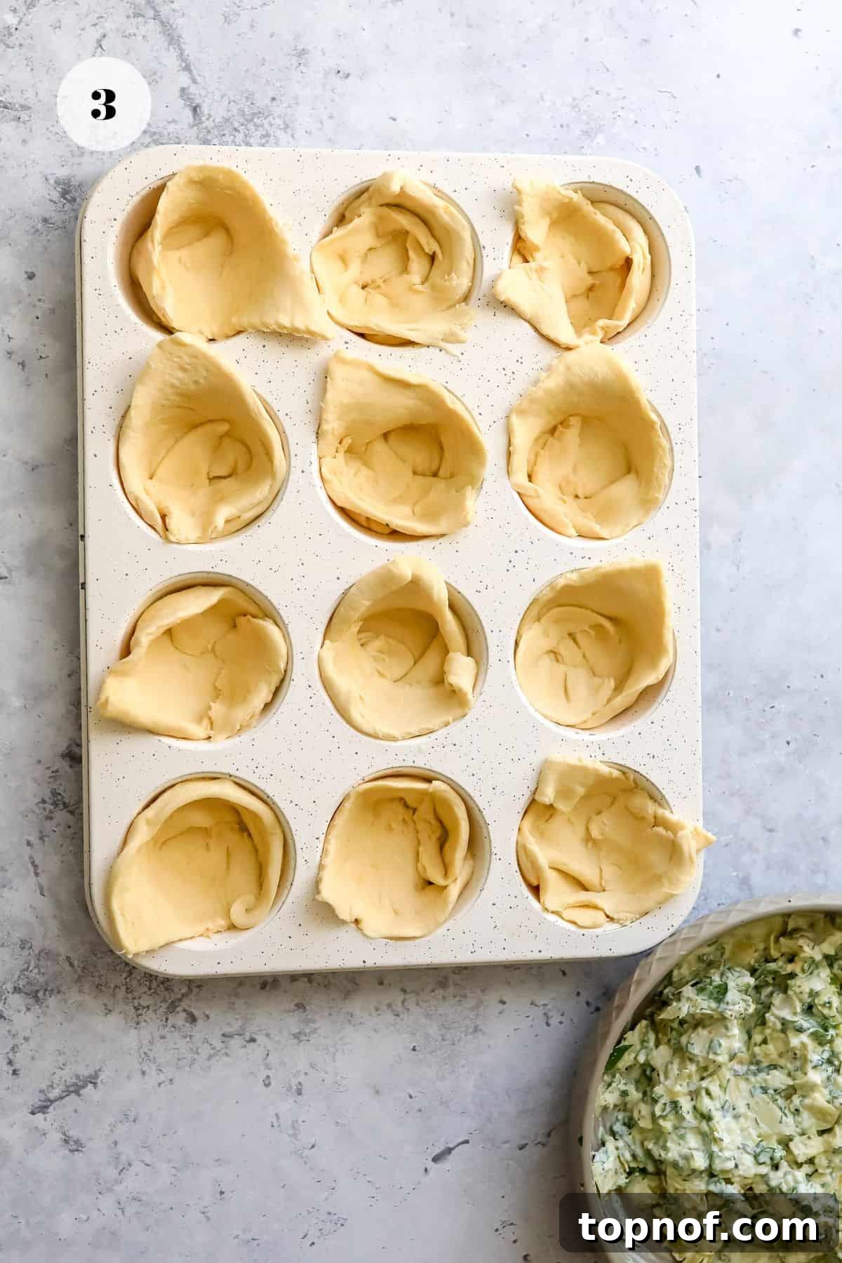 Crescent roll dough pressed into a muffin tin, creating cups for the filling.