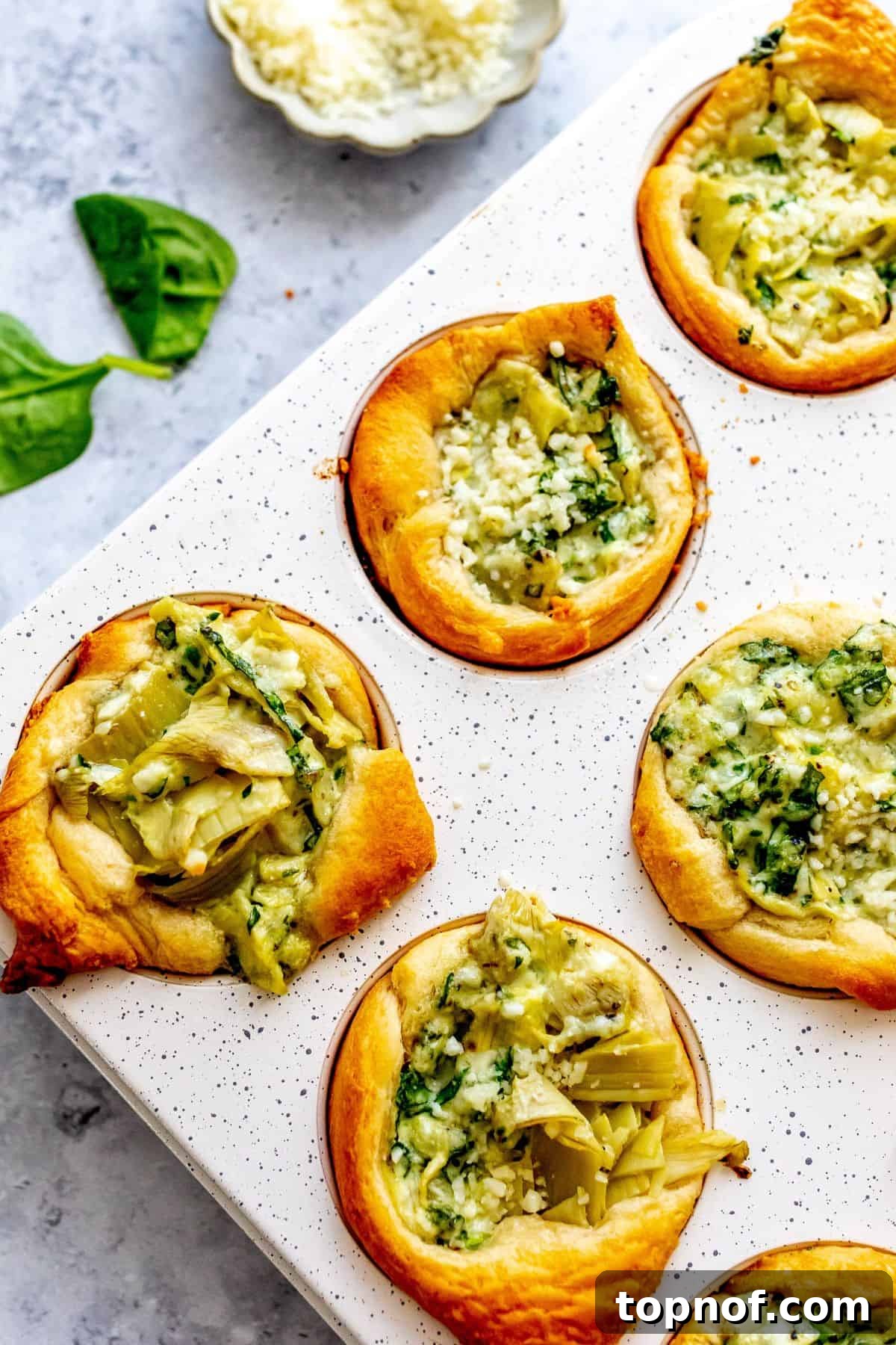 Close-up of baked Spinach Artichoke Dip Bites in a white muffin tin, showing golden crust and melted cheese.
