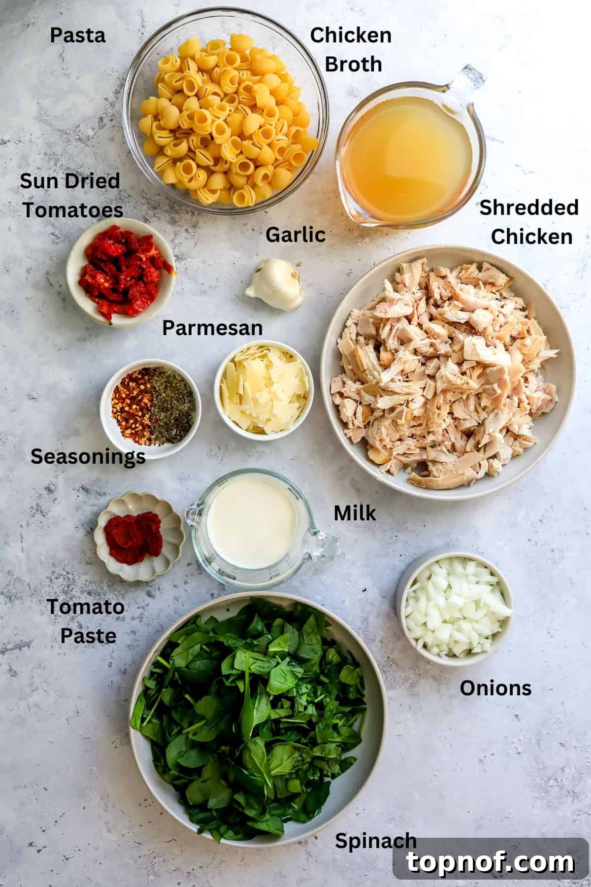 Velvet Vows Chicken Soup 3 Fresh ingredients for Marry Me Chicken Soup, including onions, garlic, sun-dried tomatoes, spinach, and shredded chicken, neatly arranged on a kitchen counter.