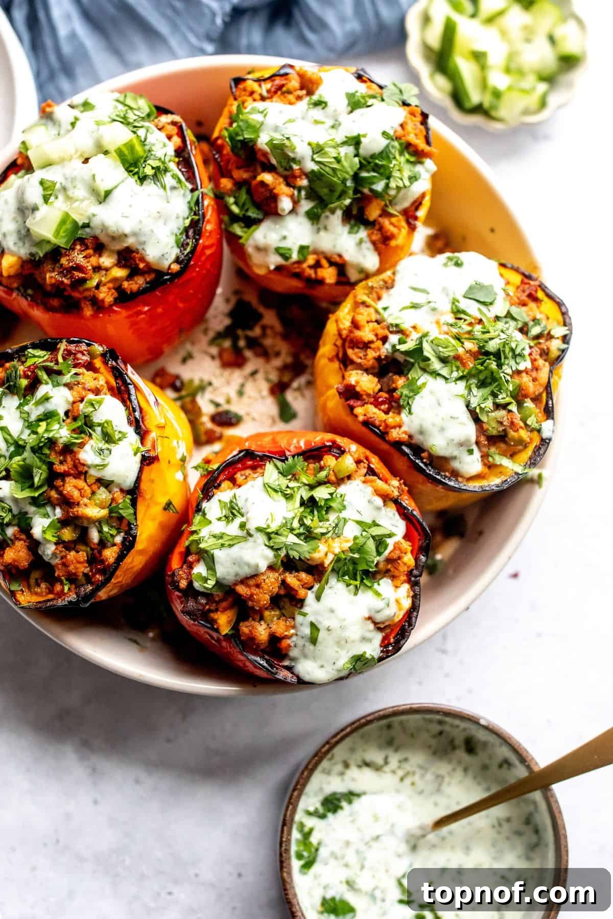 Zesty Mediterranean Turkey Stuffed Peppers 2 Delicious Mediterranean Ground Turkey Stuffed Peppers served in a grey bowl, garnished with fresh herbs, alongside elegant gold forks and plates.