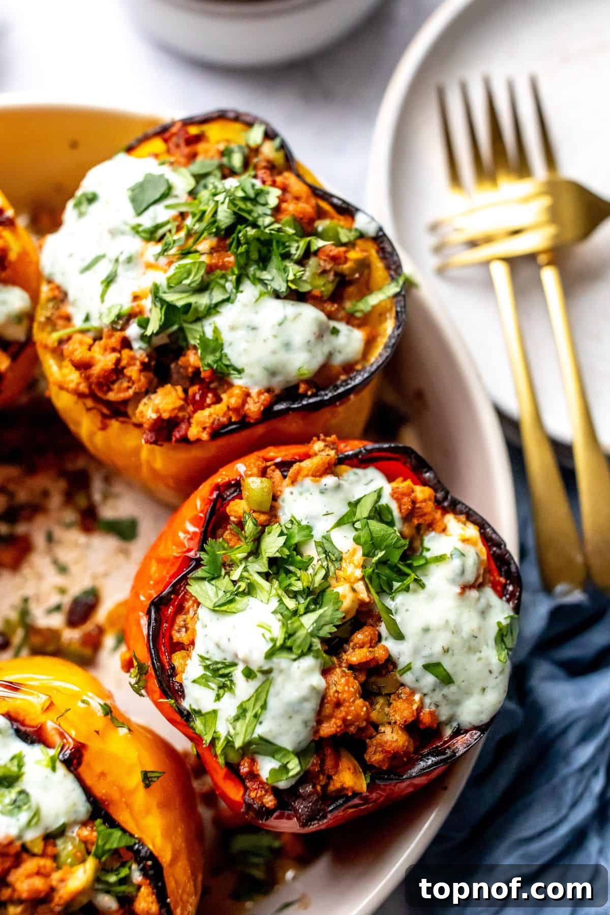 Zesty Mediterranean Turkey Stuffed Peppers 5 Close-up photo of beautifully cooked Mediterranean Ground Turkey Stuffed Peppers, garnished with tzatziki, in a grey bowl with gold forks.