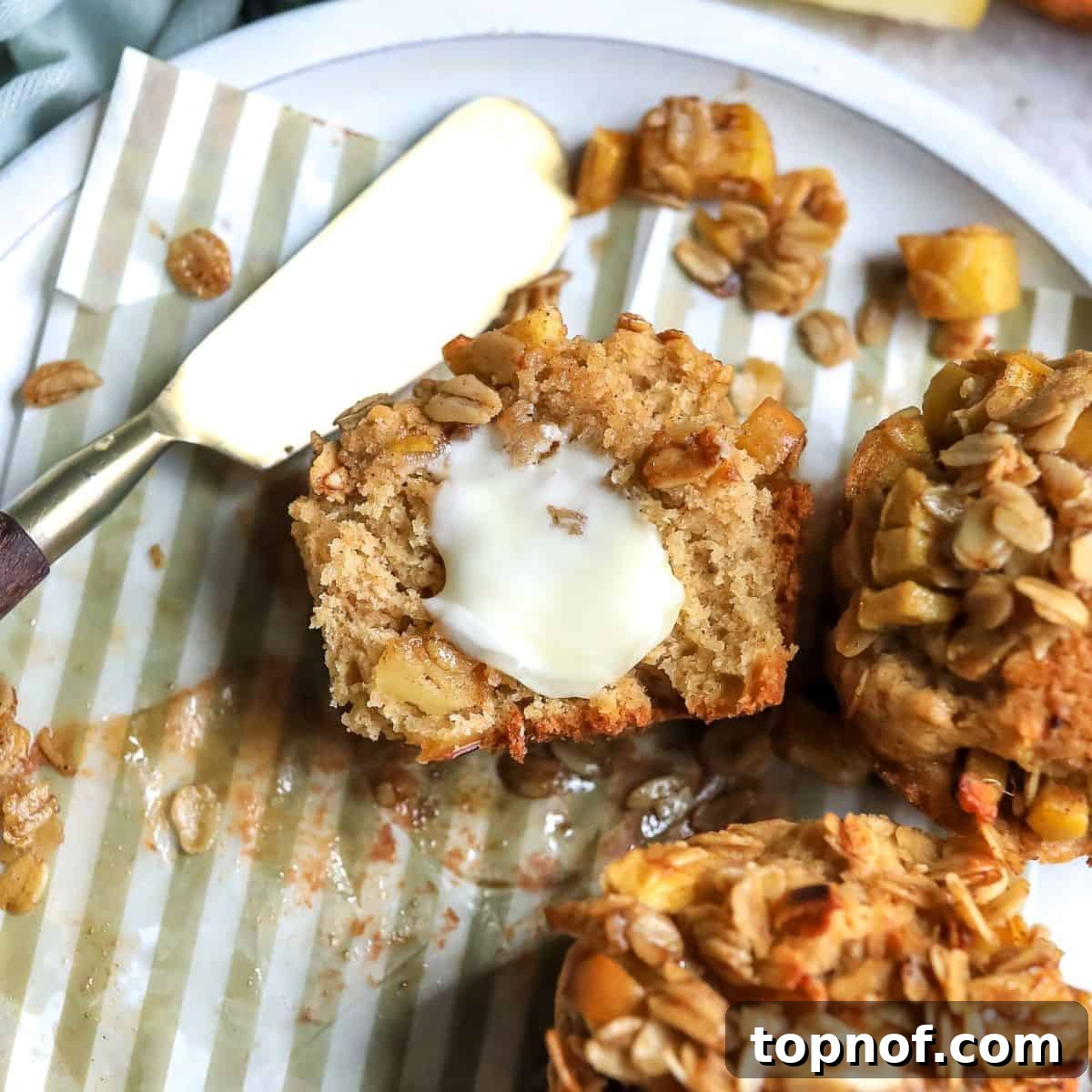 Warm Apple Cinnamon Muffins 2 Apple spice muffins elegantly arranged on a plate with fresh apples, butter, and a gold knife, highlighting their bakery-fresh appearance and crumb topping.