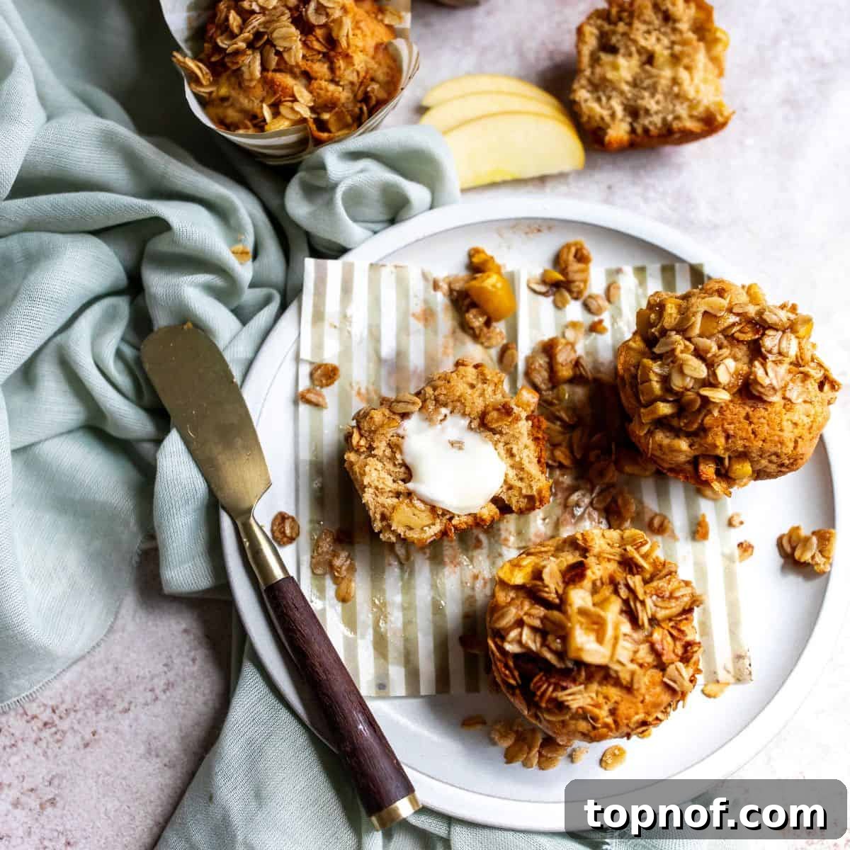 Warm Apple Cinnamon Muffins 7 Freshly baked apple spice muffins on a white plate, one sliced and served with a pat of butter, showcasing their moist interior and golden-brown streusel topping.