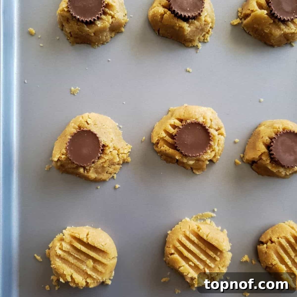 Plant-Based Peanut Butter Choc Chip Bliss 5 Raw vegan peanut butter cookie dough balls with mini peanut butter cups pressed into them, arranged on a baking sheet, ready for the oven.