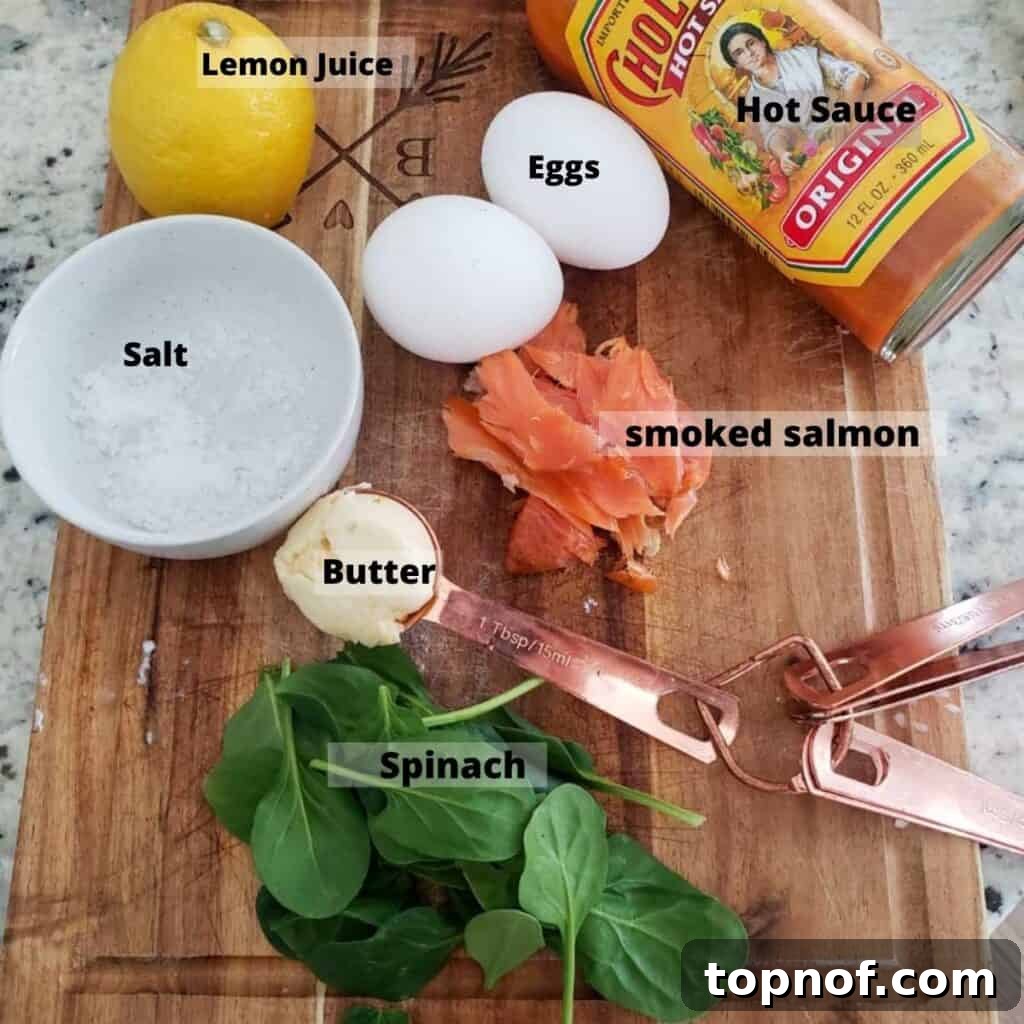 Nordic Benedict 3 A collection of fresh ingredients laid out for Smoked Salmon Eggs Benedict, including large eggs, vibrant green spinach, a package of smoked salmon, a lemon, a stick of butter, and a bottle of hot sauce.