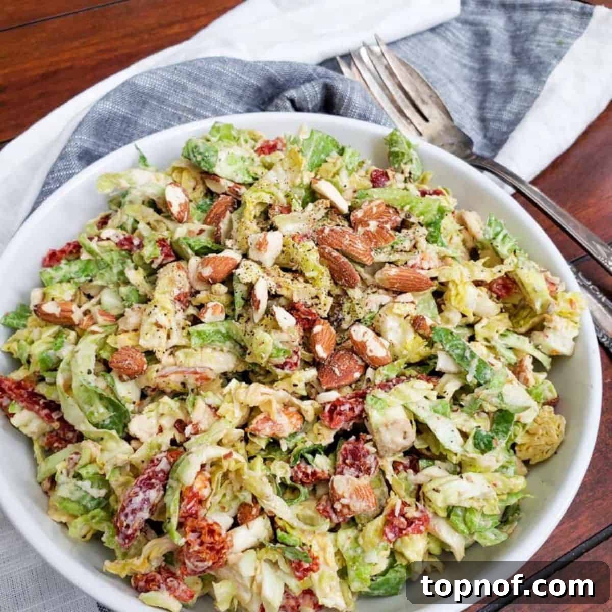 Brussels Ribbon Salad 2 Shaved Brussels Sprout Salad in a white bowl, garnished with fresh herbs and a drizzle of dressing.