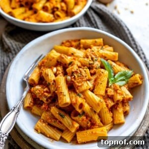 A white bowl with vibrant red pepper pesto mixed with noodles, ready to be enjoyed.