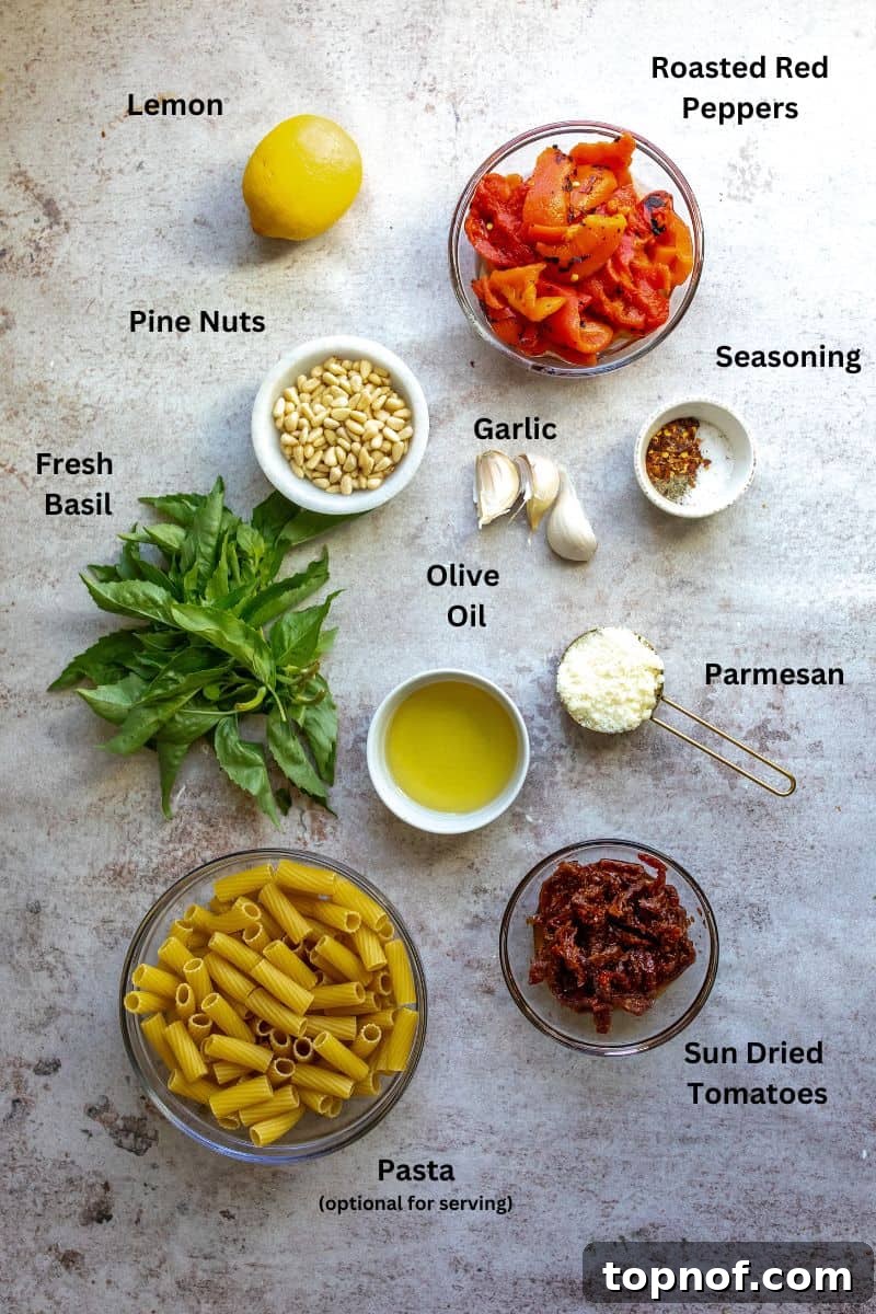 Roasted Red Pepper Pesto 3 Glass bowls holding fresh ingredients like roasted red peppers, sun-dried tomatoes, and pine nuts, alongside fresh basil leaves, all arranged on a kitchen counter.
