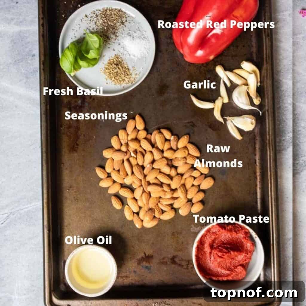 Simple Roasted Red Pepper Dip 3 A selection of fresh ingredients including red bell peppers, almonds, basil, garlic, and olive oil, laid out for making red pepper dip.
