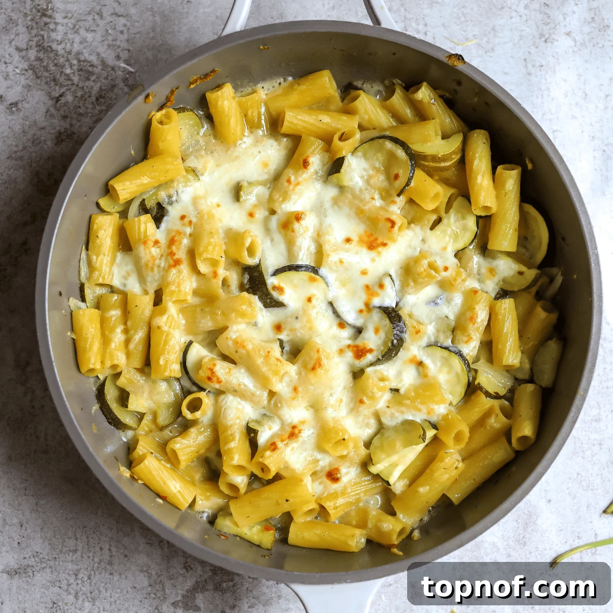 Zesty Pepper Lemon Pasta 5 A grey skillet filled with golden lemon noodles topped with perfectly melted and lightly browned cheese, fresh basil ready for serving.
