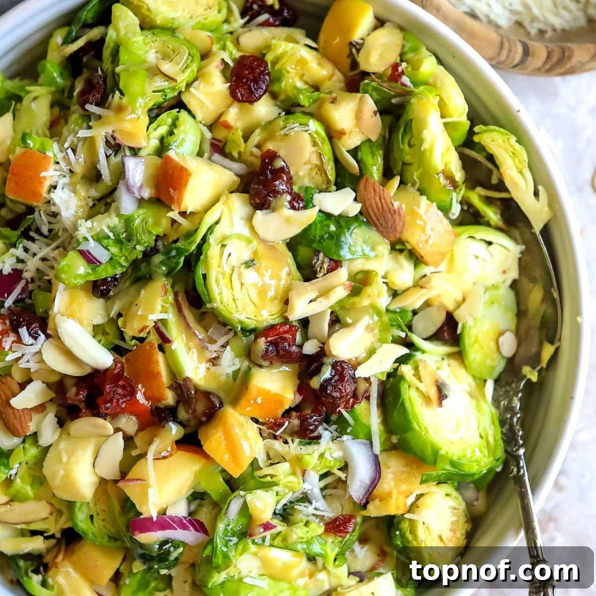 Golden Roasted Brussels Sprout Salad 6 Close-up of a ceramic bowl filled with roasted Brussels sprout salad, showing the texture of the sprouts, apples, nuts, and cheese, with a large serving spoon.