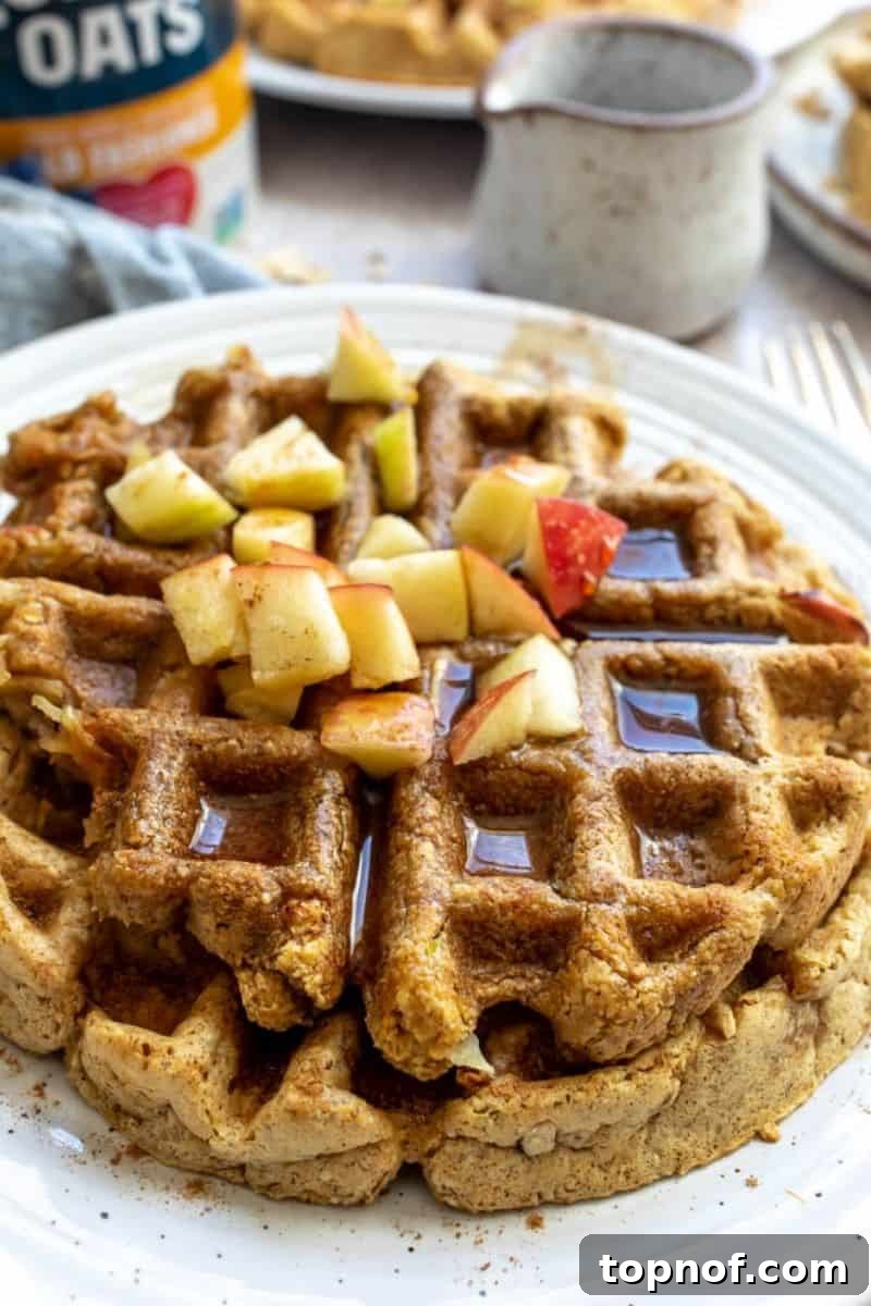Apple Pie Waffles 8 A close-up photo of a stack of apple waffles, generously drizzled with maple syrup and topped with fresh apple slices, showcasing a tempting breakfast.