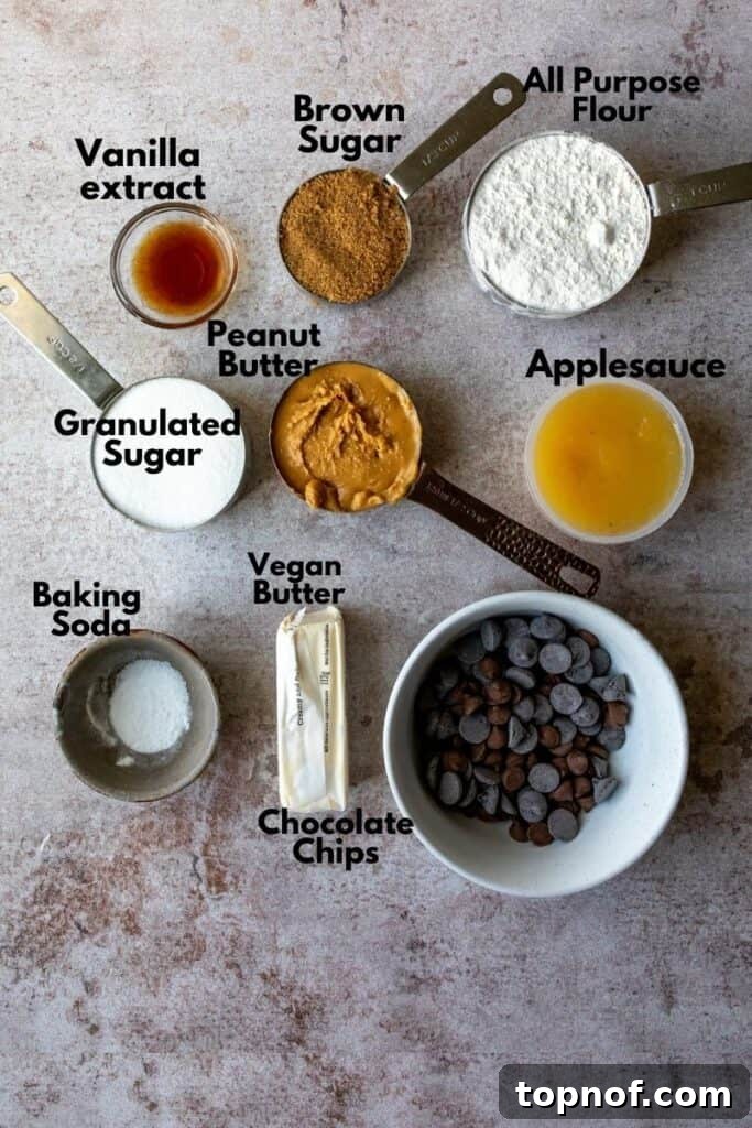 A flat lay of essential ingredients for making a homemade Chocolate Chip Peanut Butter Skillet Cookie, including flour, two types of sugar, unsweetened applesauce, vegan butter, and generous portions of chocolate chips and peanut butter.