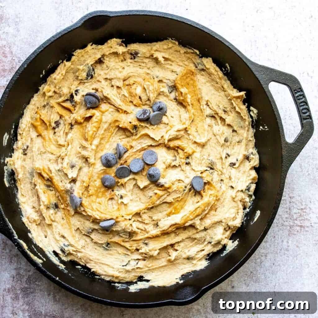 Raw chocolate chip peanut butter cookie dough spread evenly in a black cast iron skillet, perfectly prepared and ready to be baked to a golden brown perfection in the oven.