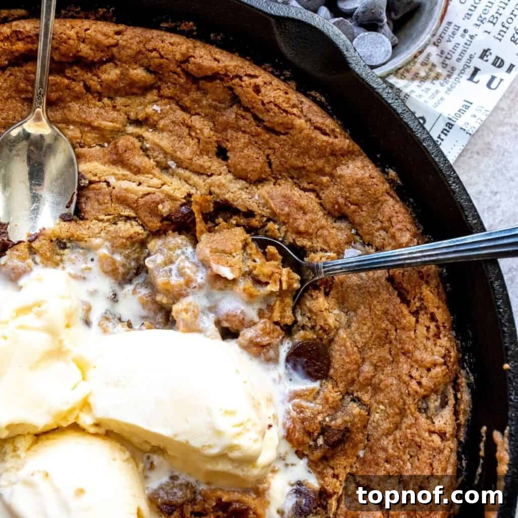 An enticing close-up of a warm, rich Vegan Chocolate Chip Peanut Butter Cast Iron Cookie in its skillet, generously topped with melting vanilla ice cream, showcasing its delicious texture and gooey centers.