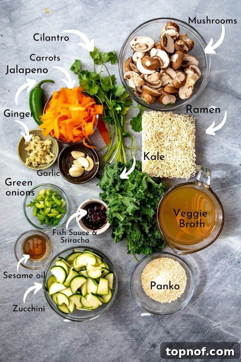 Various homemade ramen ingredients, including fresh ginger, garlic, mushrooms, carrots, kale, ramen noodles, and sauces, neatly arranged on a gray surface.