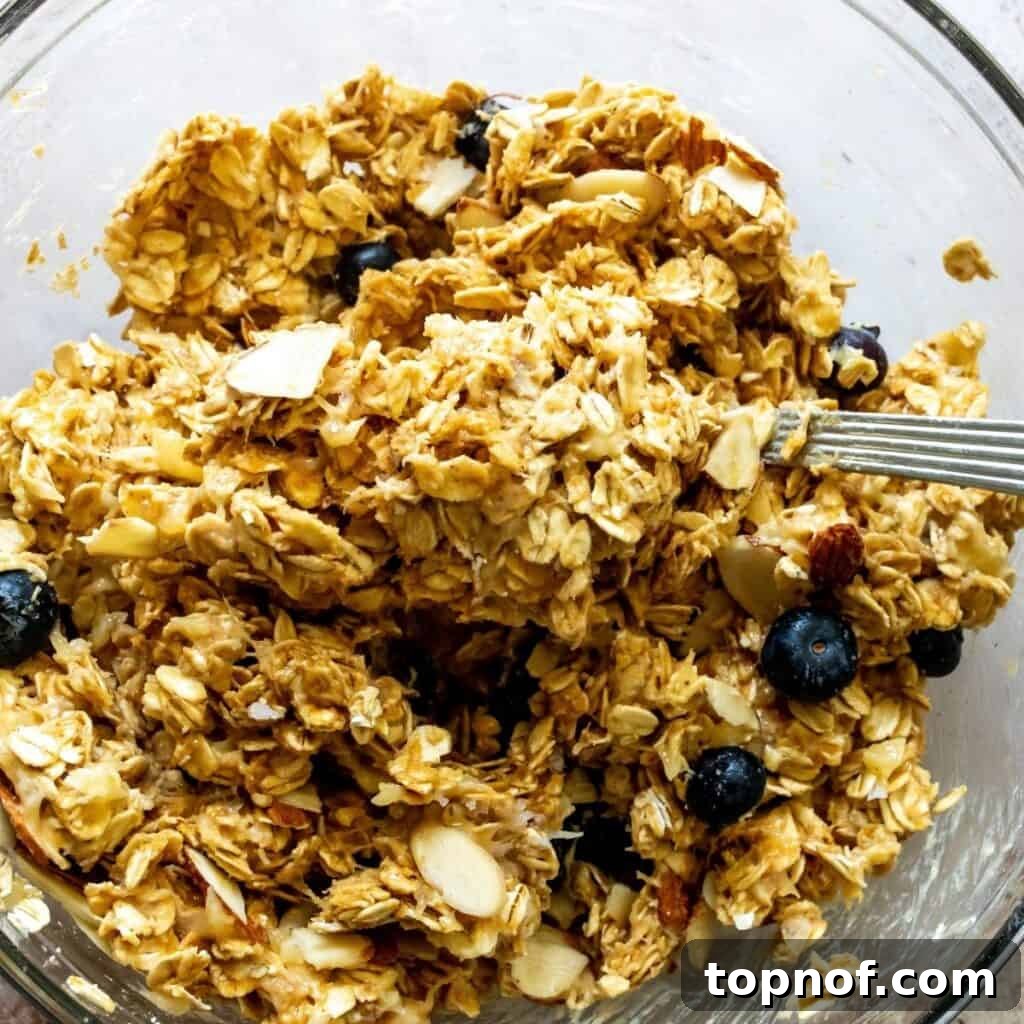 Wholesome Blueberry Oat Delights 4 A glass bowl filled with sticky breakfast cookie dough, featuring visible oats, blueberries, and almond pieces.