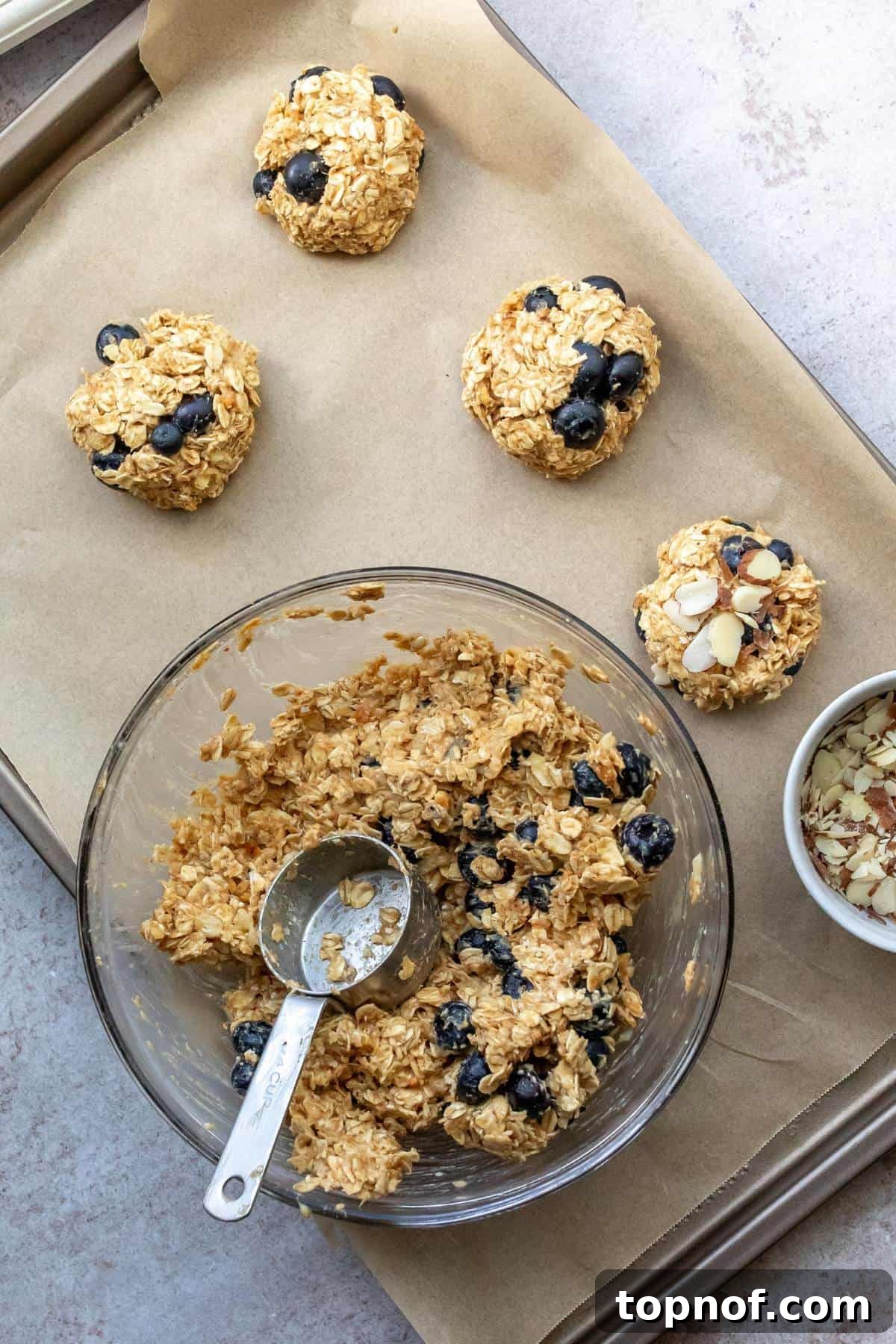 Wholesome Blueberry Oat Delights 5 A glass bowl holding the remaining blueberry oat cookie mix, with freshly shaped cookies arranged on a baking sheet to the side.