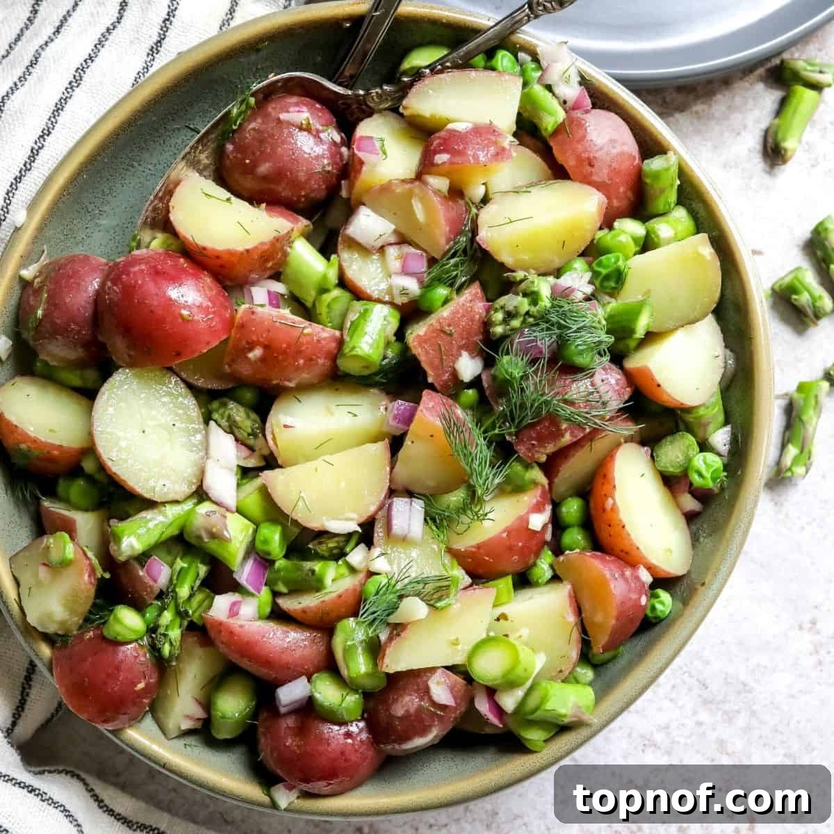 Close-up of a vibrant green bowl filled with mustard potato salad, highlighting the fresh asparagus, peas, and a creamy mustard vinaigrette. A spoon is resting in the bowl, ready to serve.