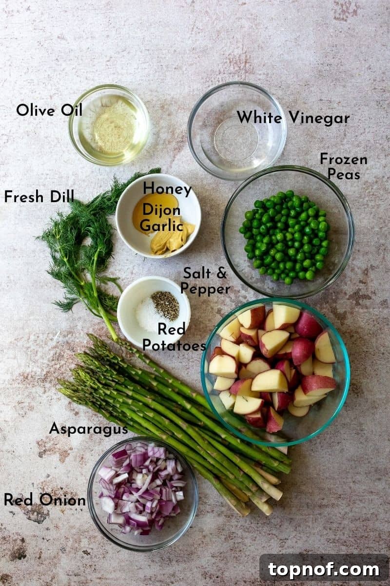 Assortment of fresh ingredients for mustard vinaigrette potato salad, including baby red potatoes, asparagus, red onion, dill, olive oil, and Dijon mustard, neatly arranged on a wooden table.