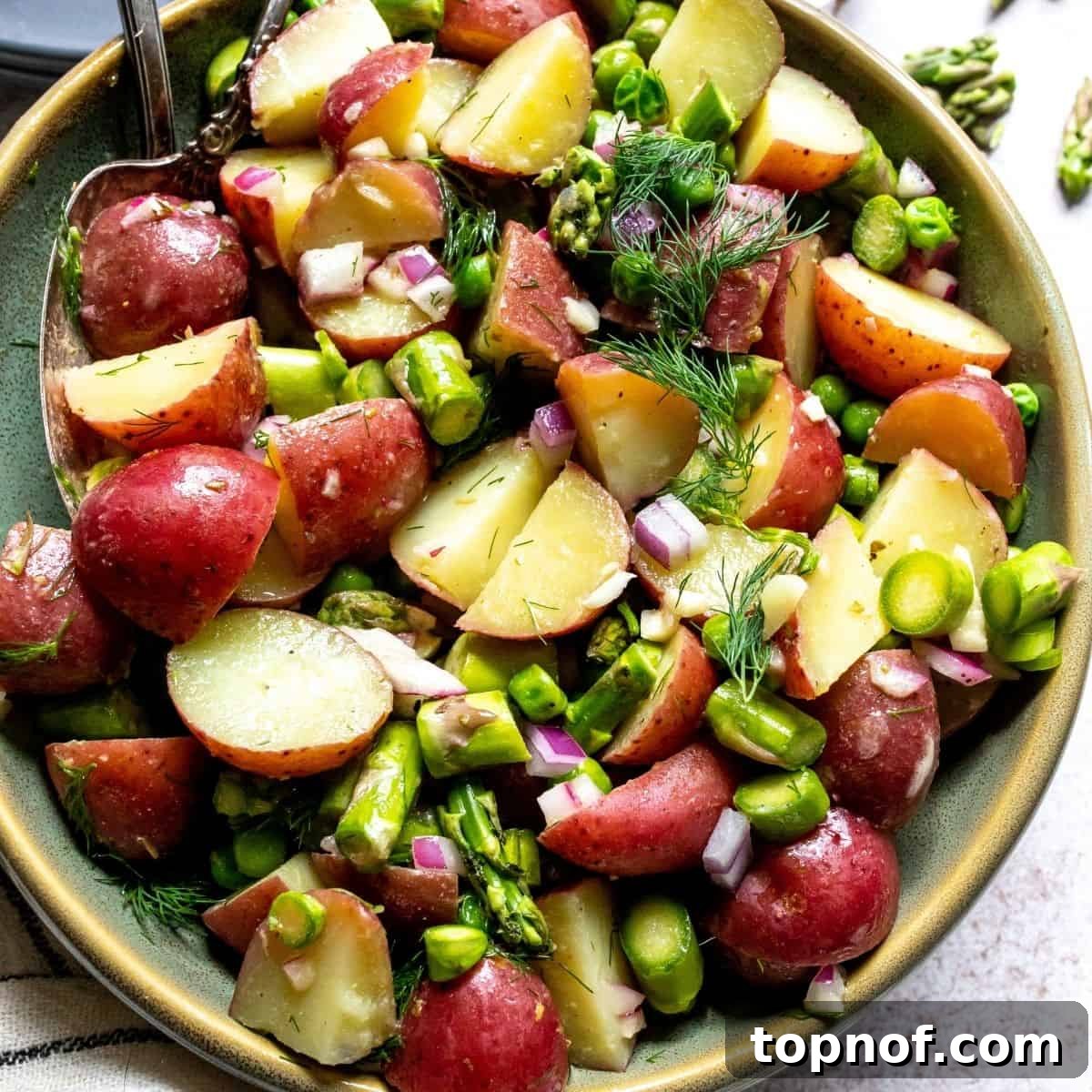 A vibrant green bowl of freshly made mustard vinaigrette potato salad, garnished with fresh dill sprigs on top, showcasing its appealing texture and color.