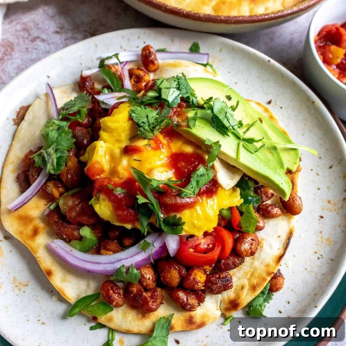 Wholesome Breakfast Tostada 2 Breakfast Tostada on a white plate with vibrant toppings including avocado, tomato, and cilantro.