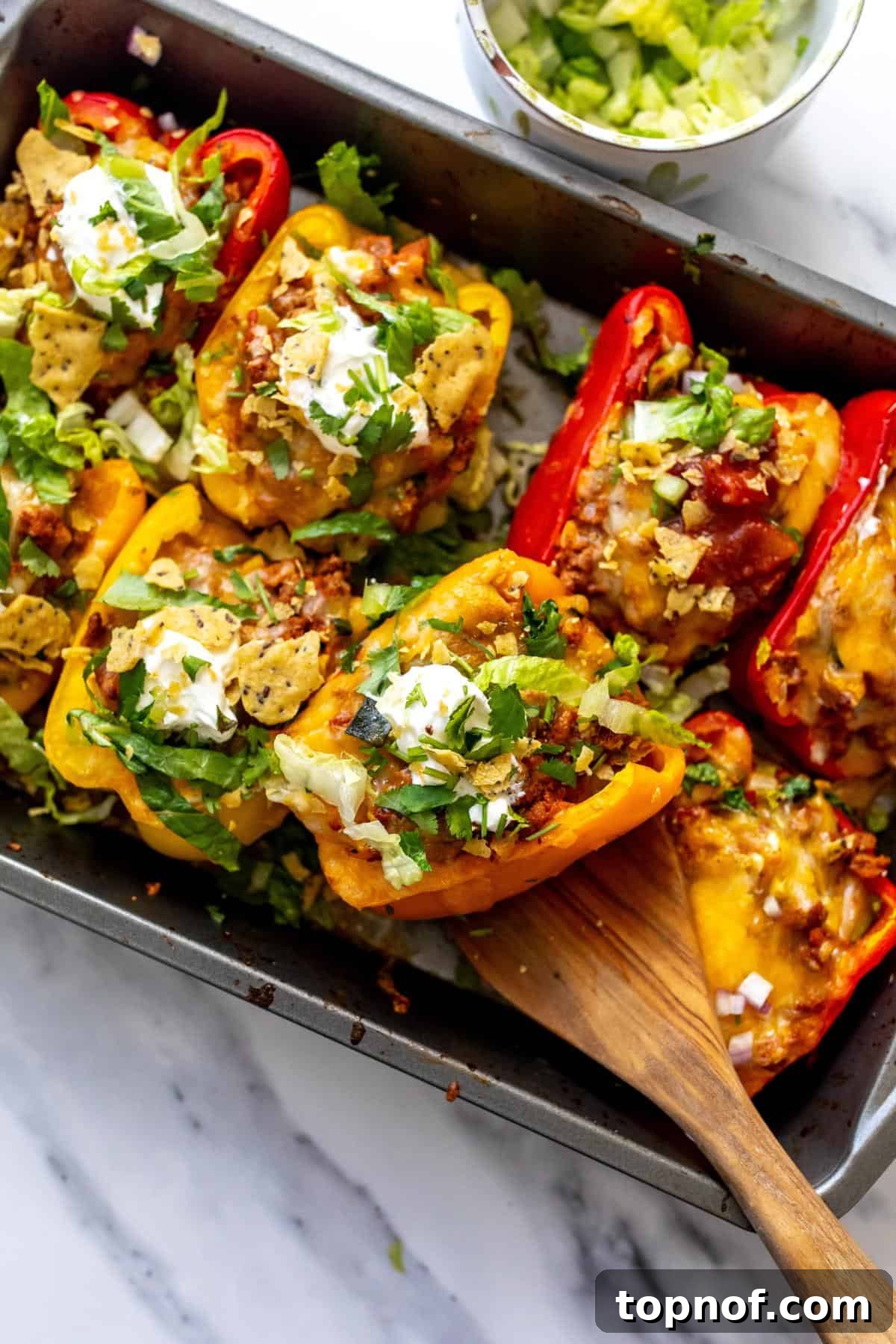 Fiesta Taco Stuffed Peppers 2 Baking dish with golden-brown taco stuffed peppers, ready to be served with a wooden spatula.