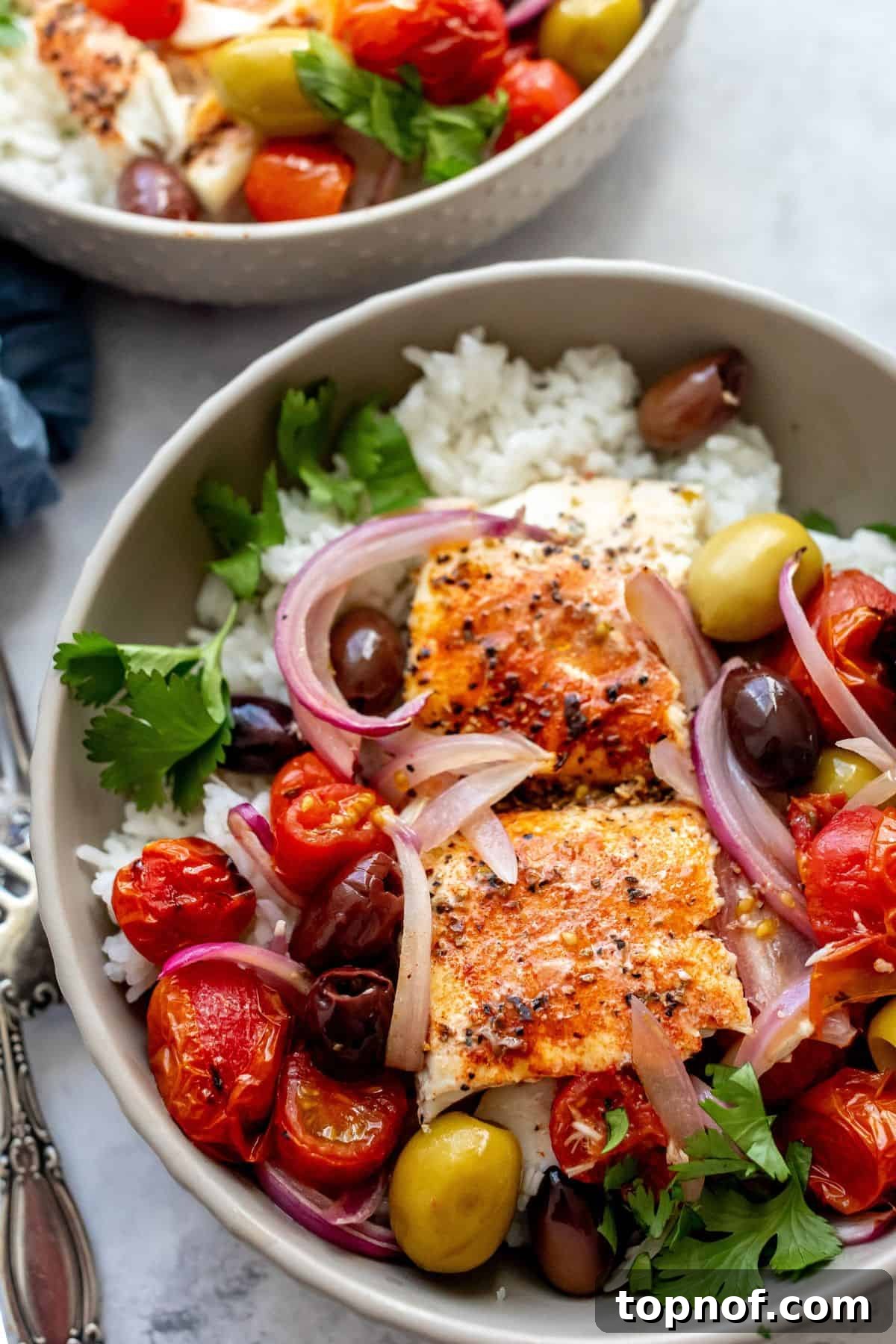 Herbed Mediterranean Fish Bake 5 Close-up of Mediterranean Baked Fish served over rice in a grey bowl, garnished with whole olives and a silver fork.