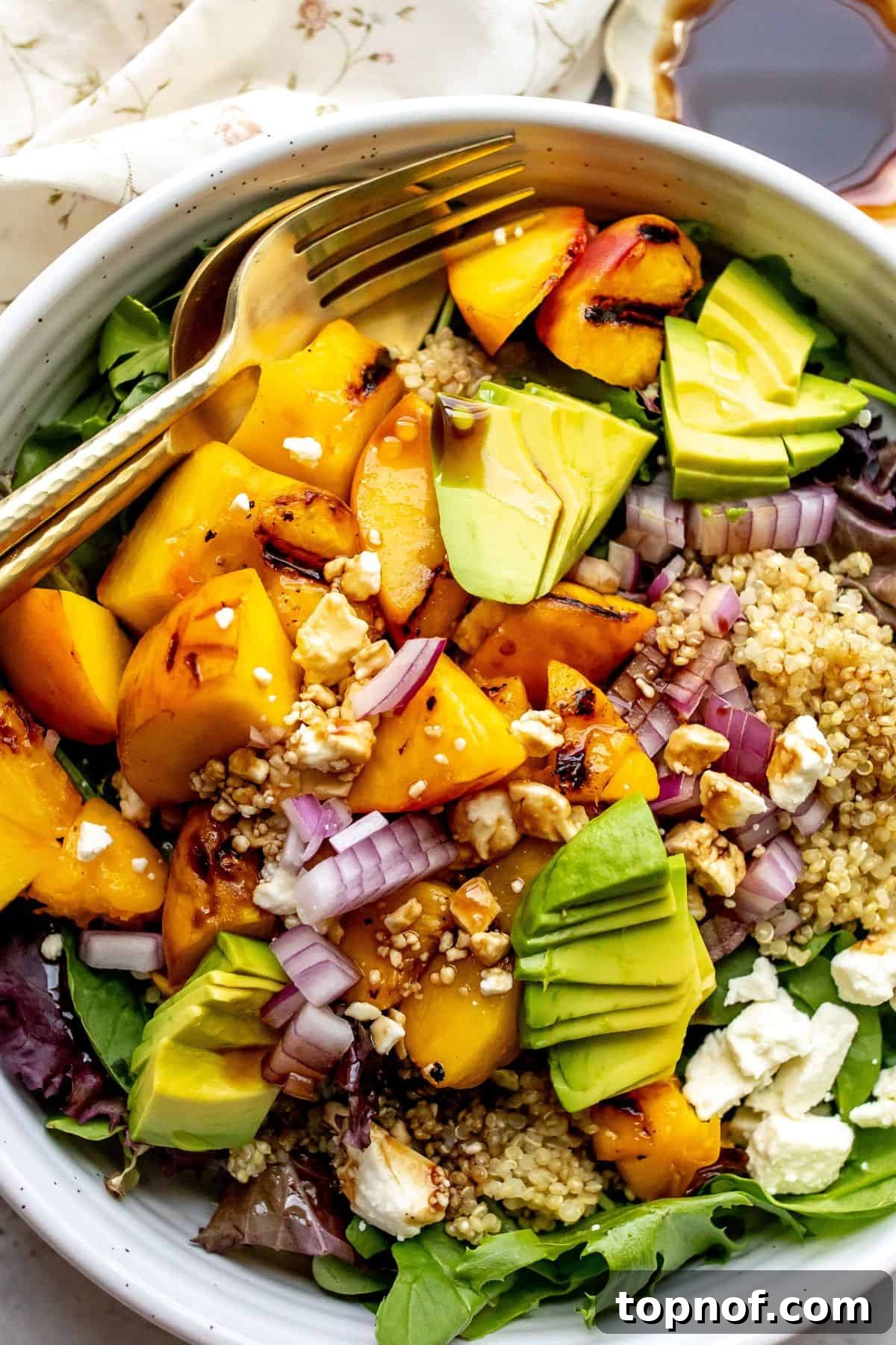 Juicy Peach and Tangy Feta Salad 5 White bowl with peach feta salad and avocado on it, serving utensils to the side.