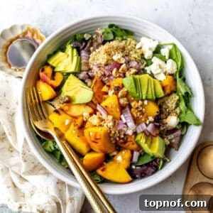 White bowl with peach feta salad and avocado on it, serving utensils to the side.