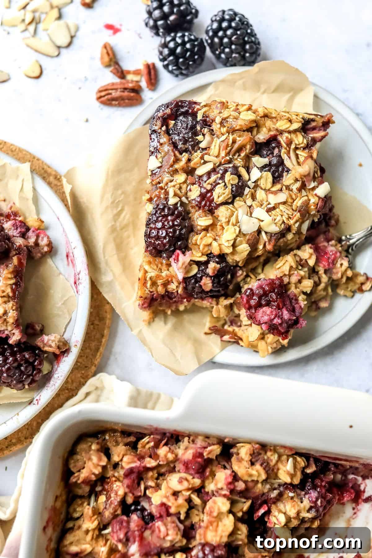 Berry Bliss Baked Oatmeal 2 A perfectly portioned square of Blackberry Baked Oatmeal on a white plate with a fork, resting on parchment paper, ready to be enjoyed.