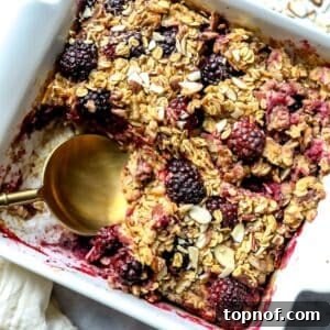 A close-up of the finished Blackberry Baked Oatmeal in a white baking dish with a spoon, highlighting its warm, inviting appearance.