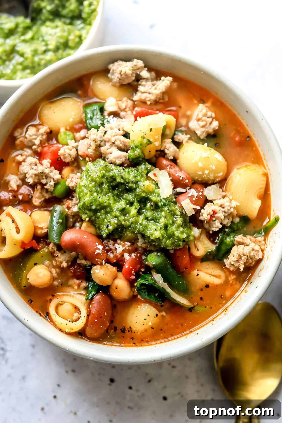 Hearty Turkey Minestrone 5 A steaming bowl of Ground Turkey Minestrone Soup, garnished with fresh pesto and grated Parmesan, served alongside a slice of crusty bread.