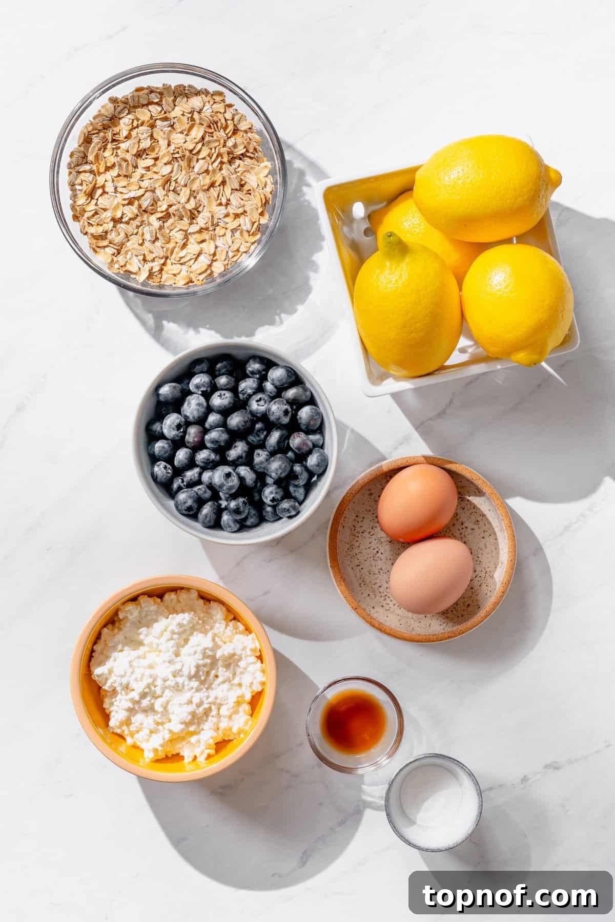 Zesty Lemon Blueberry Protein Pancakes 3 Ingredients for lemon blueberry cottage cheese pancakes including cottage cheese, eggs, rolled oats, blueberries, lemon, and baking powder arranged on a countertop, ready for blending.